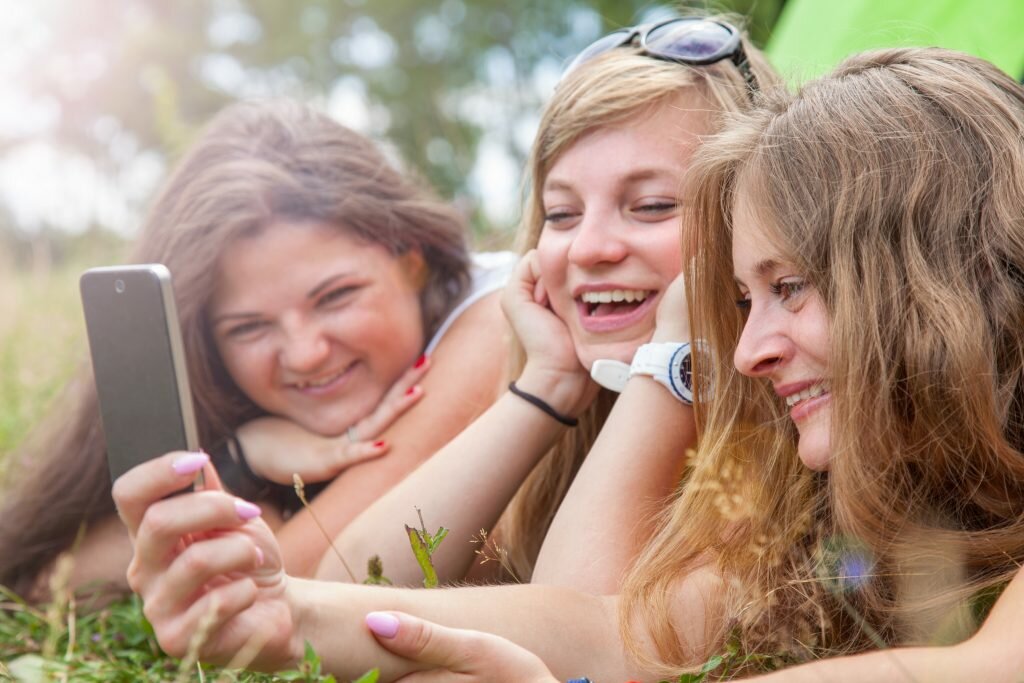 Tre skrattande flickor som ligger ner och tittar in i en smart telefon.