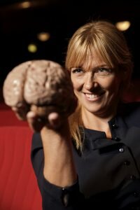 Leende kvinna som sträcker fram en hand som håller i en modell av en hjärna.